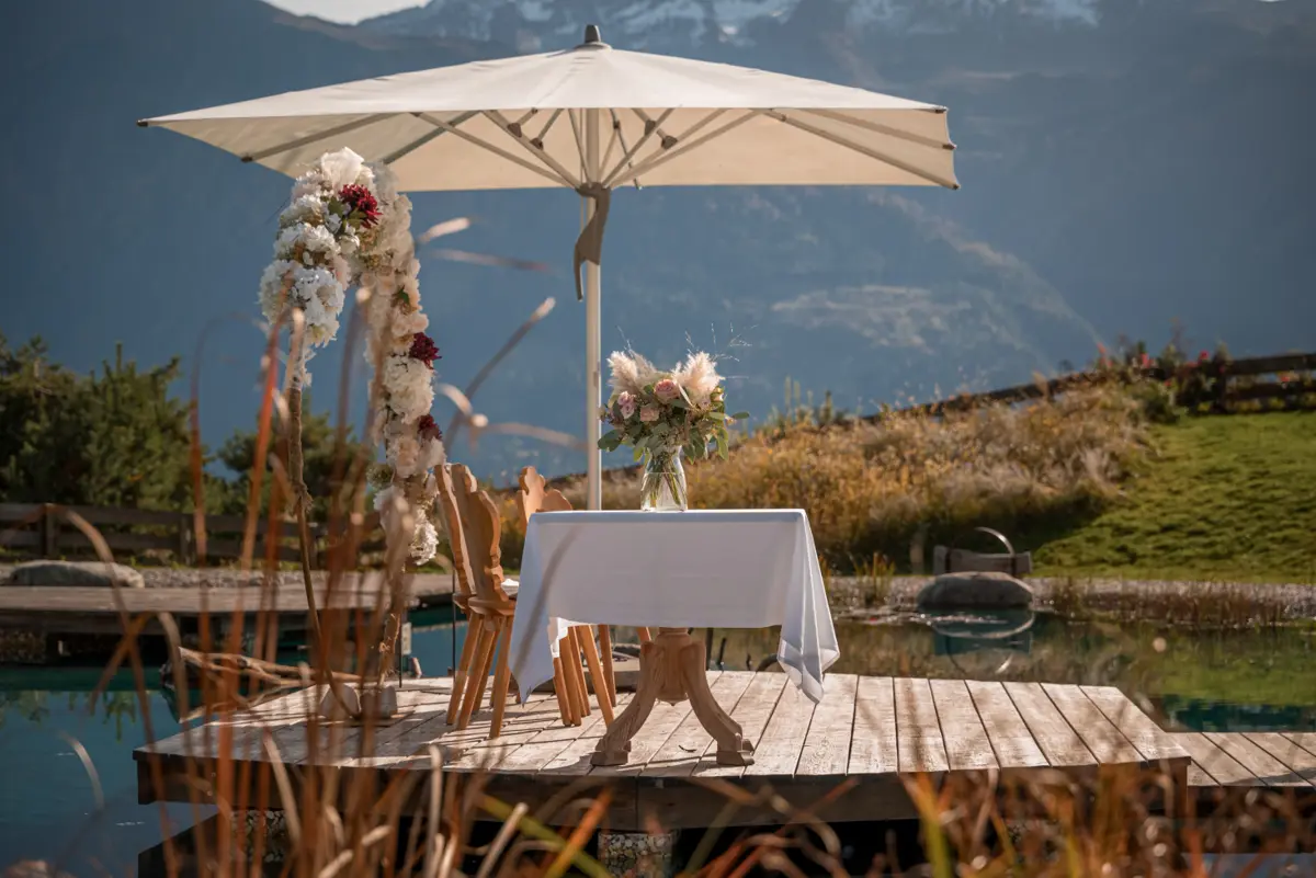 Romantisch gedeckter Tisch mit Blumenbogen auf dem Steg am Naturteich der Stöttlalm