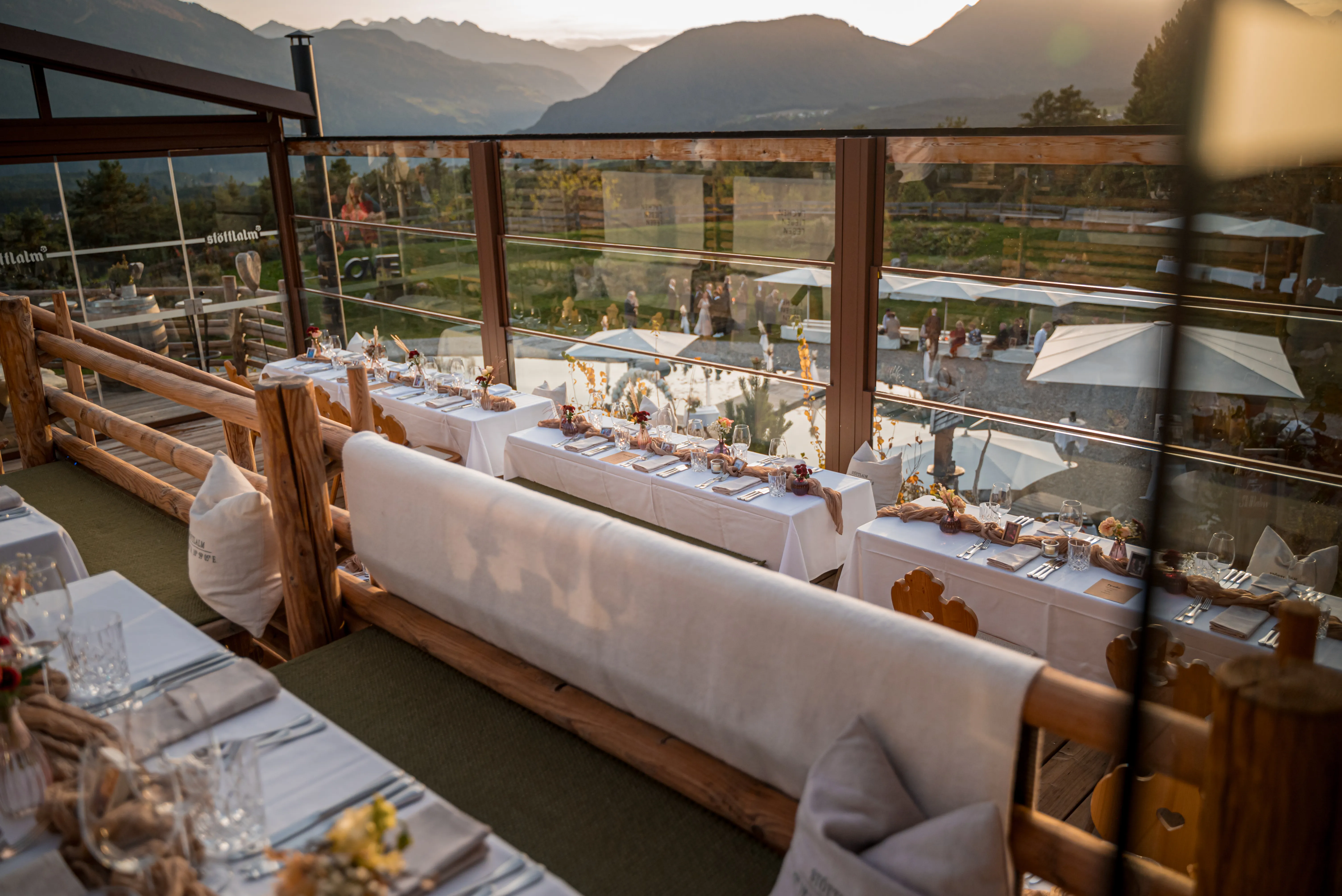 Festlich eingedeckte Hochzeitstafeln auf der verglasten Panoramaterrasse der Stöttlalm im Abendlicht
