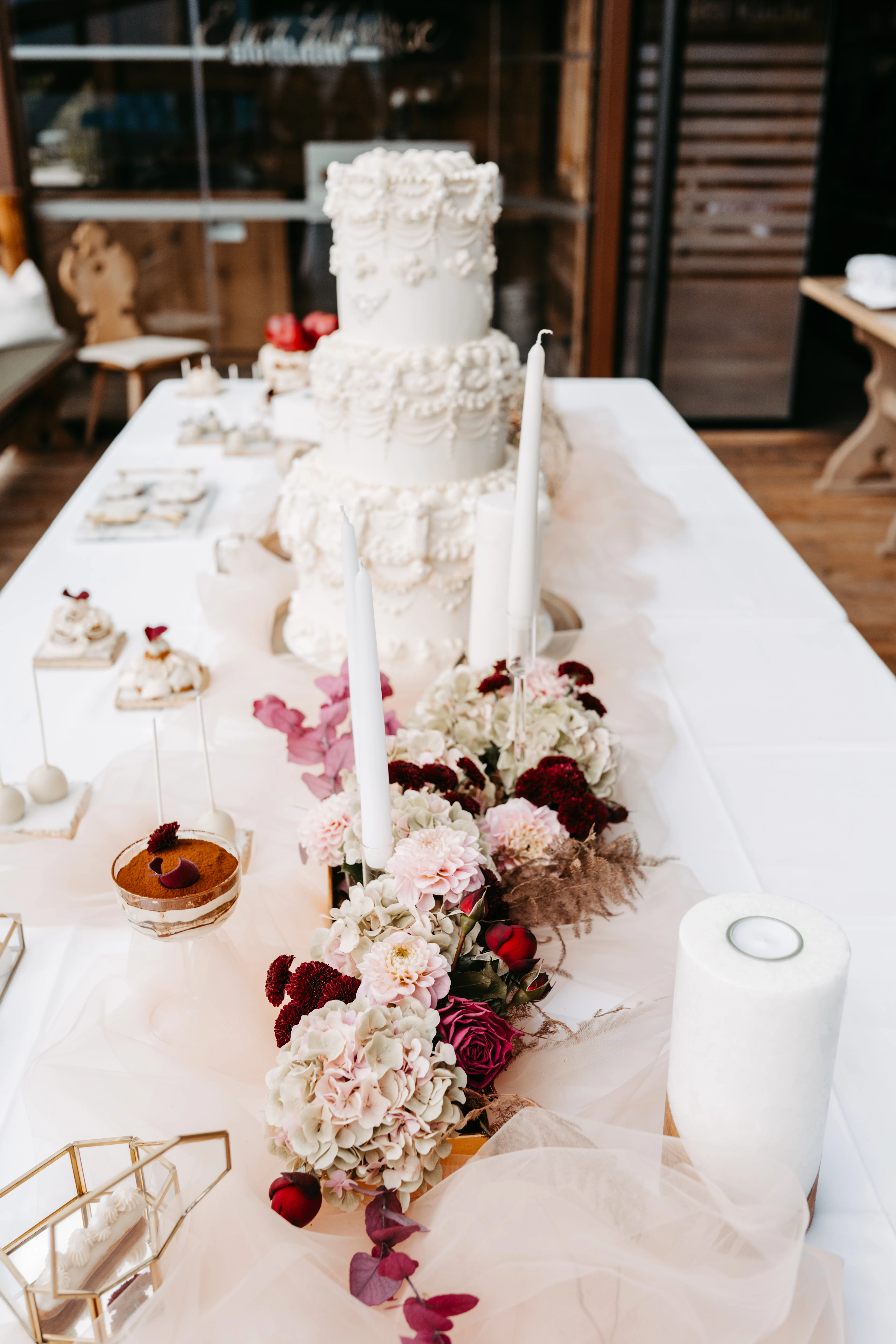 Hochzeitlicher Sweet Table mit Vintage-Hochzeitstorte und Blumengirlande vor der Holzfassade der Stöttlalm